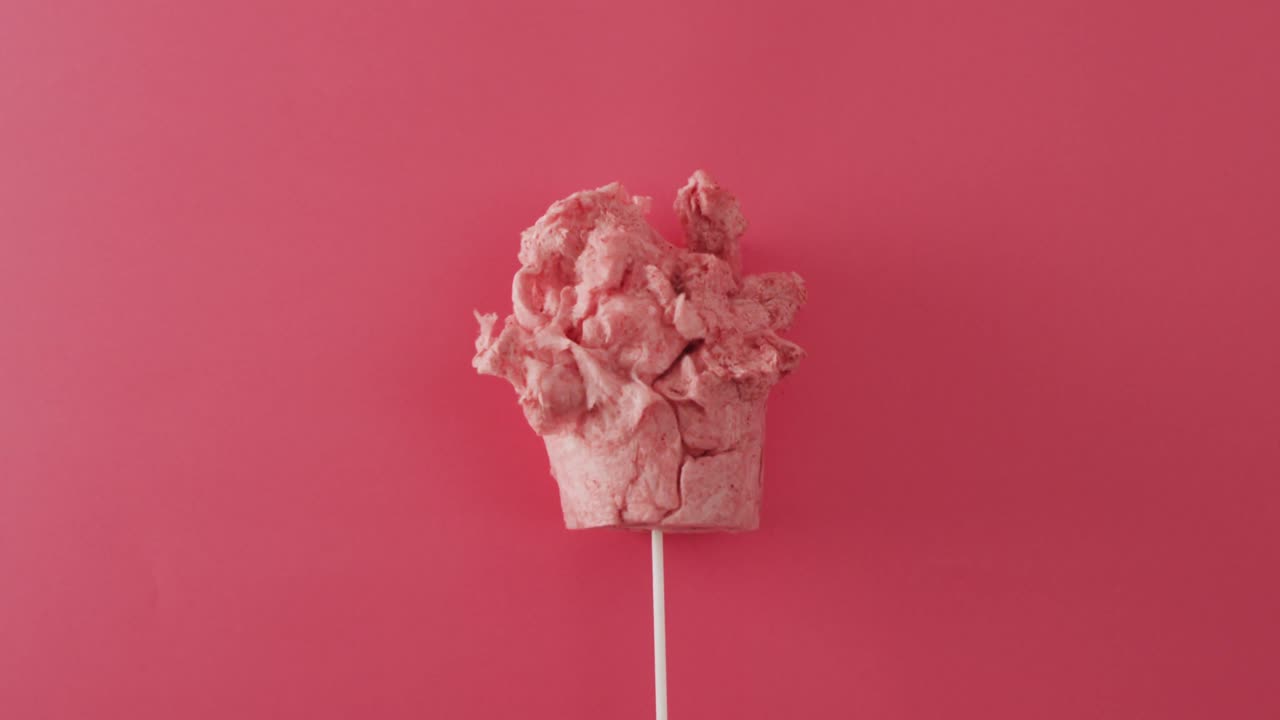 Video of marshmallow on stick lying on pink surface