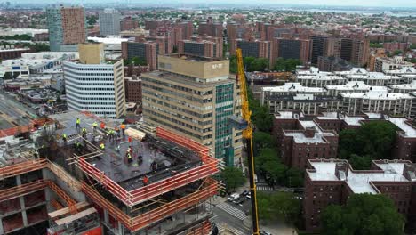 Orbiting a crane lifting construction materials to a city project site - aerial view