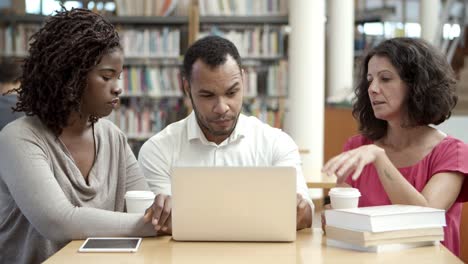 estudiantes maduros serios que trabajan con una computadora portátil en la biblioteca pública