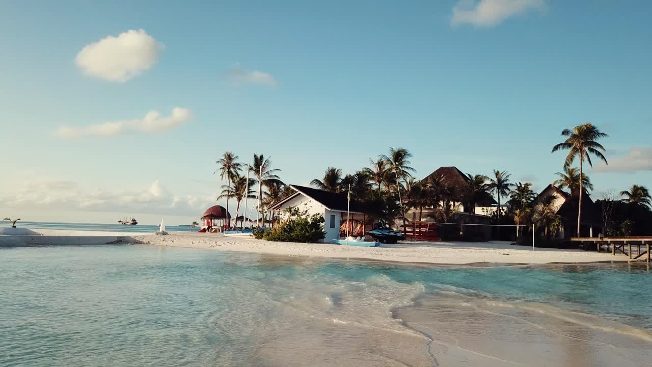 video de avión no tripulado de un complejo tropical en las maldivas, vuelo bajo, laguna azul, palmeras verdes, tiempo soleado, caja de arena, aguas poco profundas, 4k