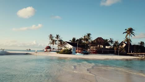 Drone-video-of-a-tropical-resort-in-the-Maldives,-low-flight,-blue-lagoon,-green-palms,-sunny-weather,-sandbox,-shallow-water,-4K