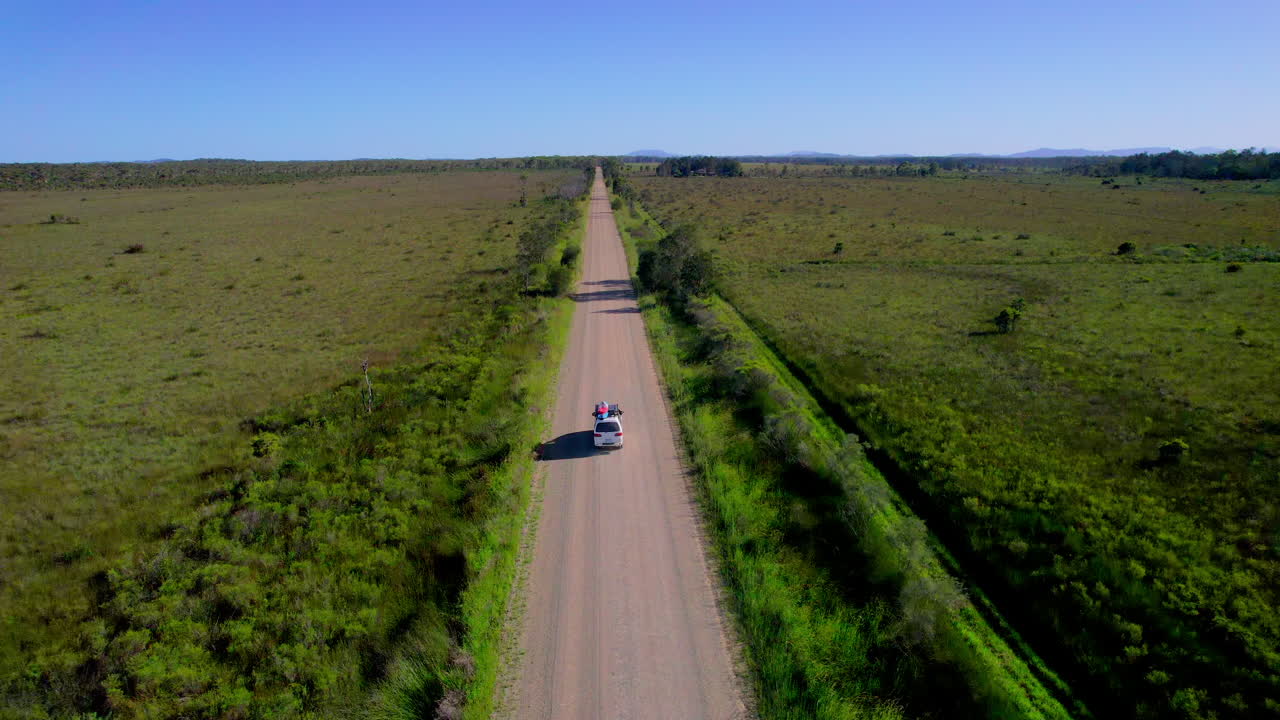 Drone follows a van driving along a gravel road flanked by lush green fields between Crescent Head and Port Macquarie, NSW. A peaceful countryside journey captured from above.