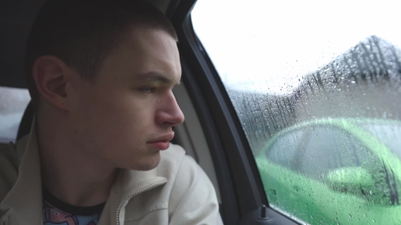 Young Man Sitting On The Backseat Of Car Looking Into The Window With Rain Drops On A Rainy Day.- close up shot