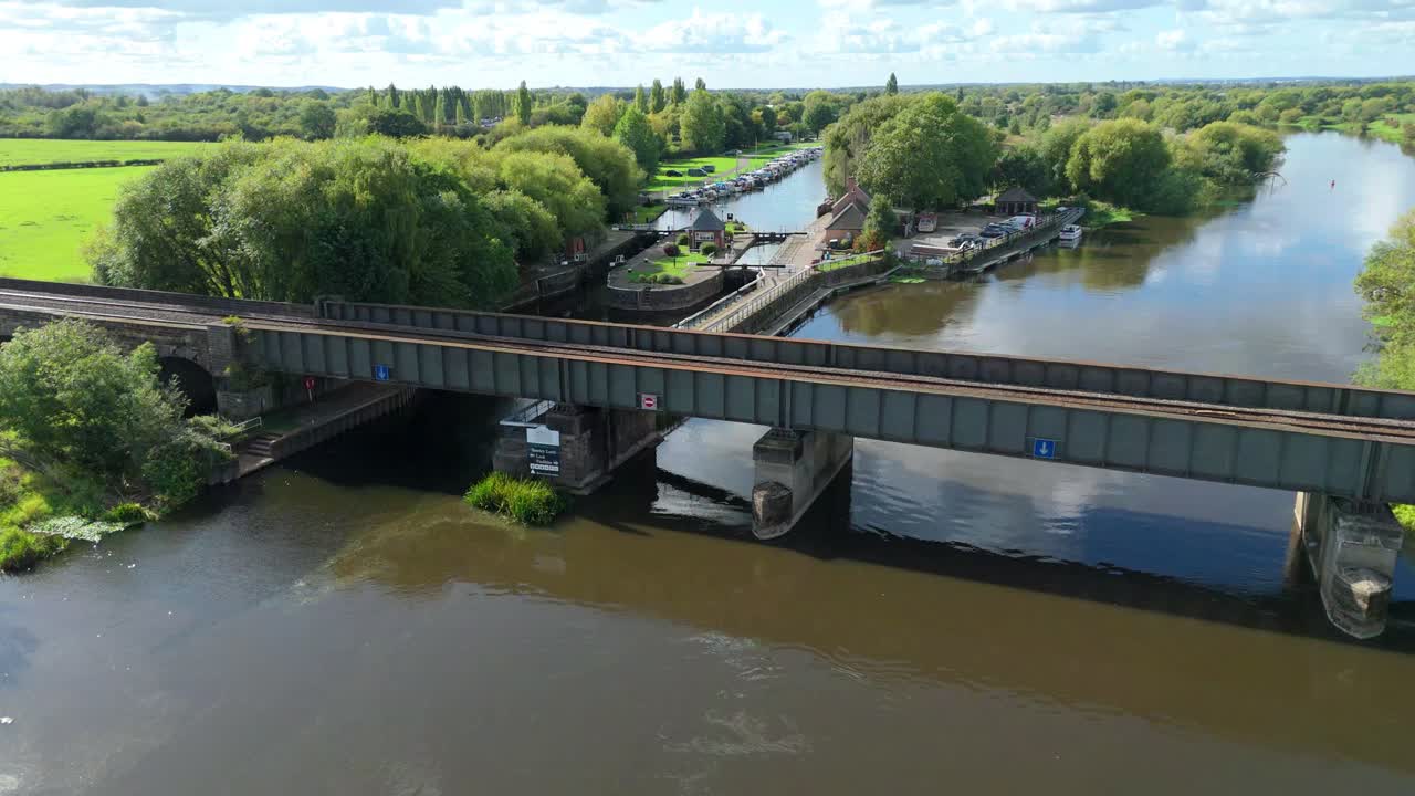 high up drone shot of bridge crossing a river with green landscapes and canal boat locks in England