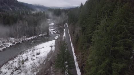 Road-leading-through-forest-and-mountains-next-to-a-river-in-winter