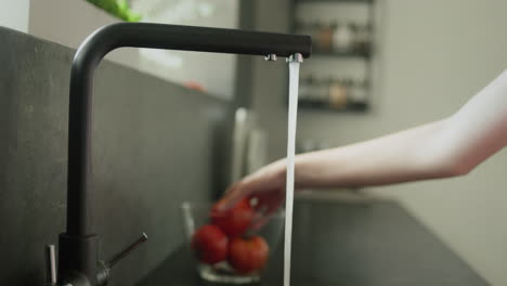 women's hands wash a tomato under running tap water.