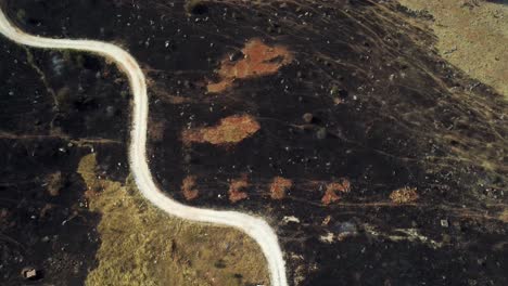 Top-down-cinematic-view-of-road-in-burnt-down-grazing-land-destroyed-by-wildfires-in-northern-Greece,-August-2023