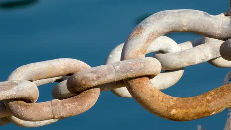 Close-up-of-rusty-chains-in-port-of-Blanes-against-blue-water-background