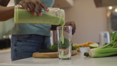 Manos-De-Una-Atractiva-Mujer-Afroamericana-Vertiendo-Batido-Casero-En-Un-Vaso-En-La-Cocina