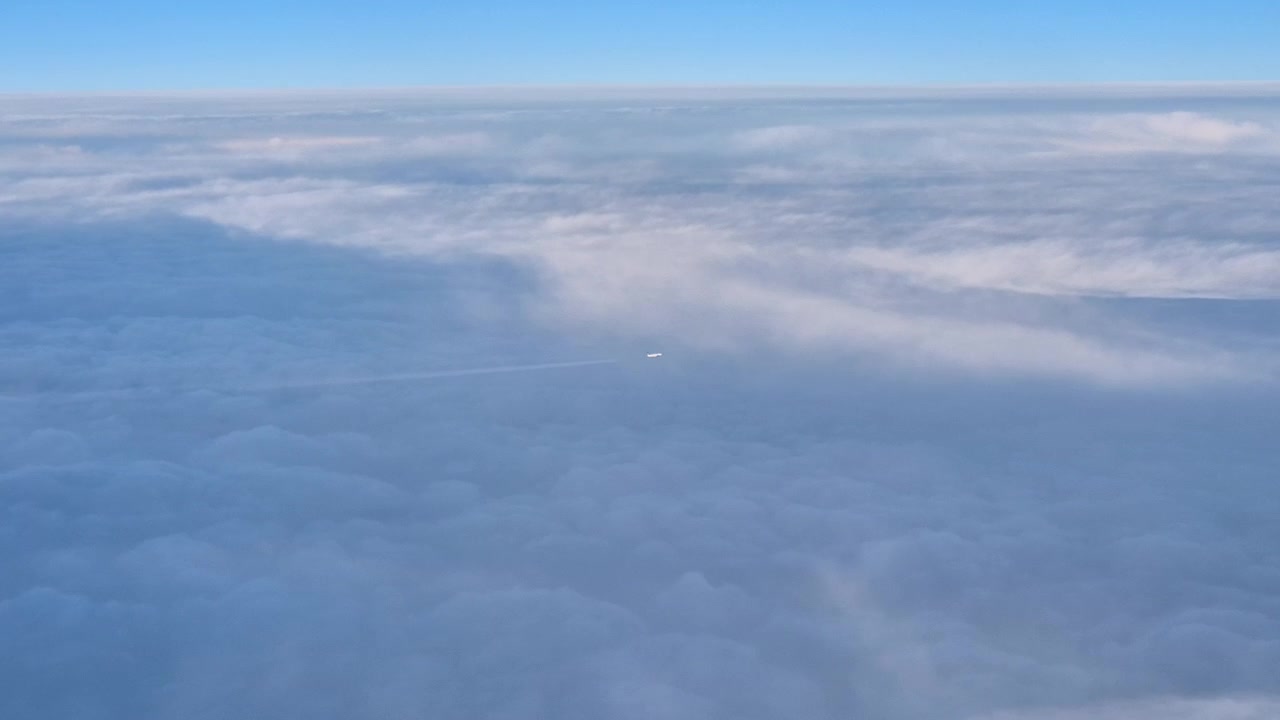 Udsigt fra et flyvindue af et andet fly, der flyver over skyerne.