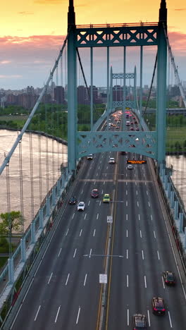 numerous cars moving quickly along triborough bridge in new york. football pitch and car park on both sides from the bridge. cityscape under beautiful pink sky at backdrop. vertical video