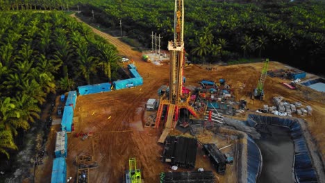 imágenes cinematográficas de drones de 4k de la estructura del equipo de la plataforma de perforación en tierra para la exploración y explotación de petróleo en medio de la jungla rodeada de palmeras durante la puesta de sol y el alto precio del petróleo