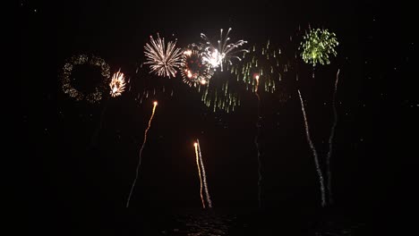 Fireworks-firing-from-water-surface-and-exploding-on-night-sky-with-glowing-stars,-water-reflections,-and-firework-sparkle-trails-3D-animation