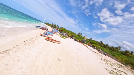 Dynamic-fpv-flight-over-turquoise-Caribbean-Sea,-golden-beach-with-boats-and-green-scenery-during-summer