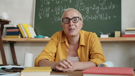 female teacher speaking on camera via online call from classroom