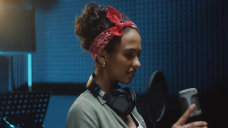 portrait of young beautiful woman singer standing at the mic in the recording sound studio and smiling to the camera happily