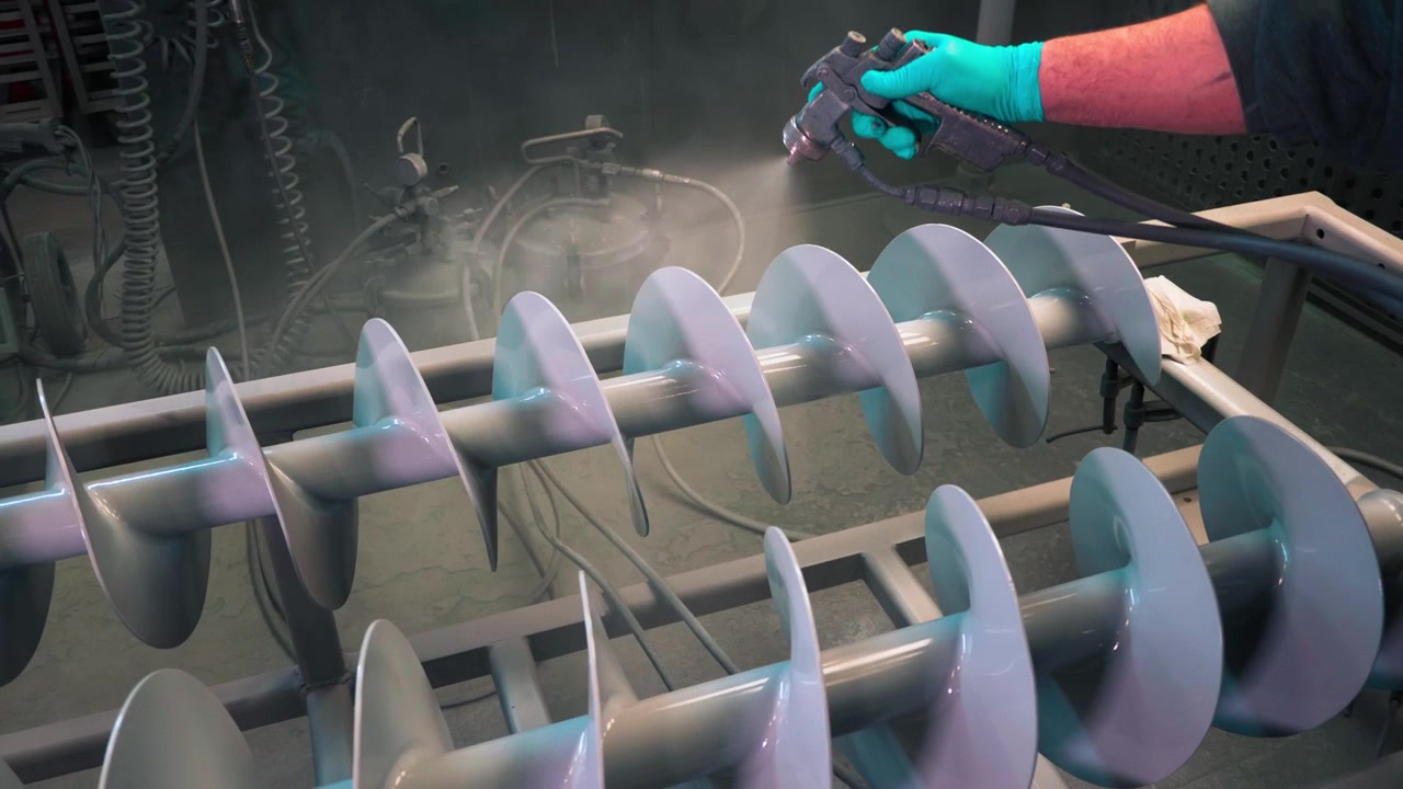 Application of white anti-corrosion powder coating to metal industrial rotors with stray gun in a plant.