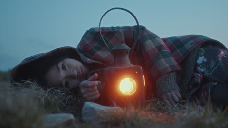 young pensive woman resting in meadow with lantern during twilight hour