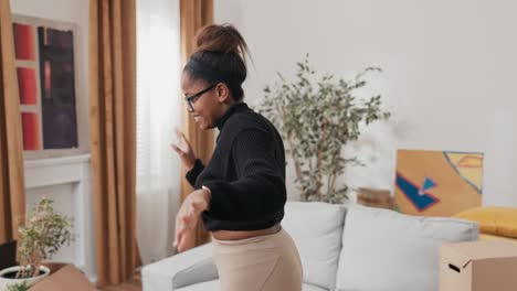 una mujer feliz bailando en el medio de la habitación, aplaudiendo, balanceándose al ritmo de la música, la alegría de haberse mudado a un apartamento alquilado comprado cajas de cartón con cosas empacadas