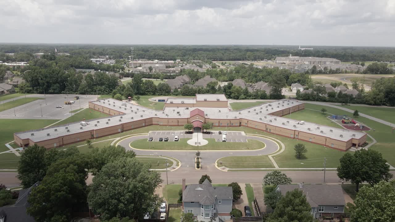 A drone zoom-in shot capturing a suburban neighborhood in the United States, showcasing tree-lined streets and residential houses. The greenery and -planned layout highlight the peaceful.