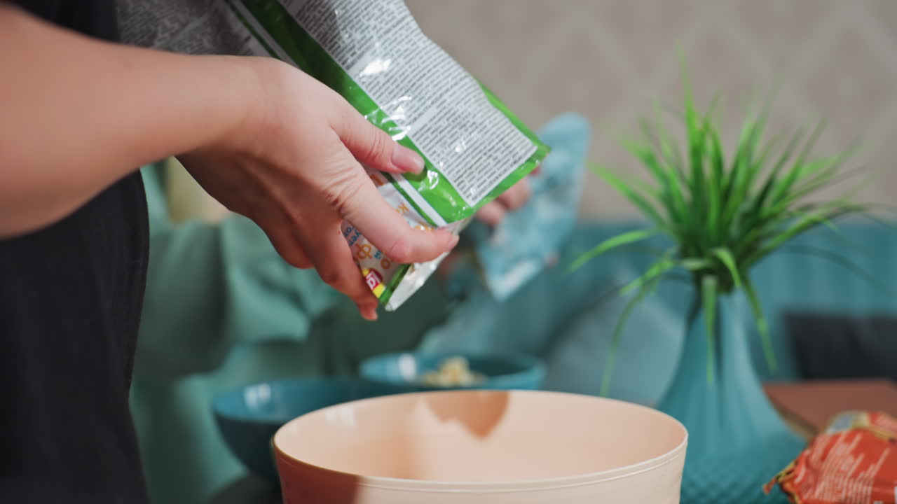 close up of young women friends in kitchen pouring corn flakes from bag into bowl together, casual cozy home moment, modern kitchen with appliances, social food preparation activity