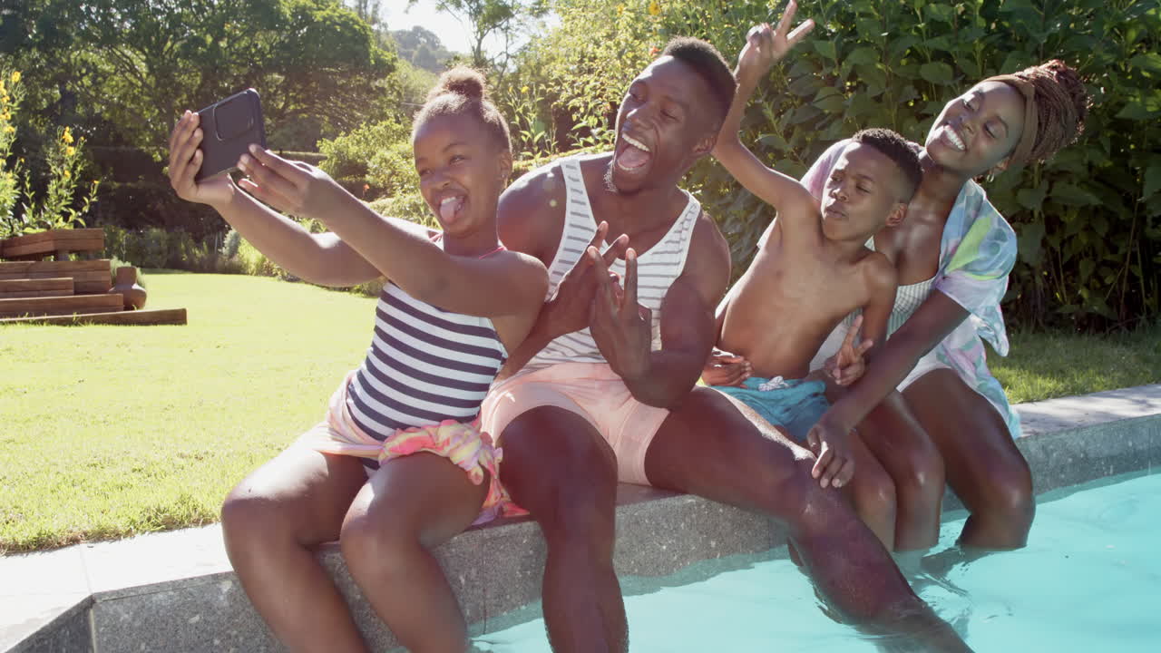 Famiglia afroamericana che si fa un selfie, seduta a bordo piscina e che si gode la giornata estiva insieme