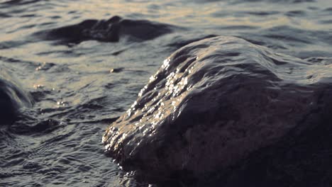 imágenes de cerca y en cámara lenta de ondas de agua de mar del océano que golpean una roca durante la puesta o puesta del sol con la luz que se refleja de las rocas y el agua en resolución extremadamente alta en calidad de resolución 4k