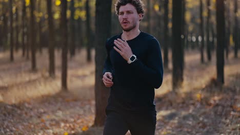 Close-up-shot-of-a-man-with-curly-hair-in-a-black-sports-uniform-running-quickly-during-his-morning-jog-in-the-autumn-forest-in-the-morning