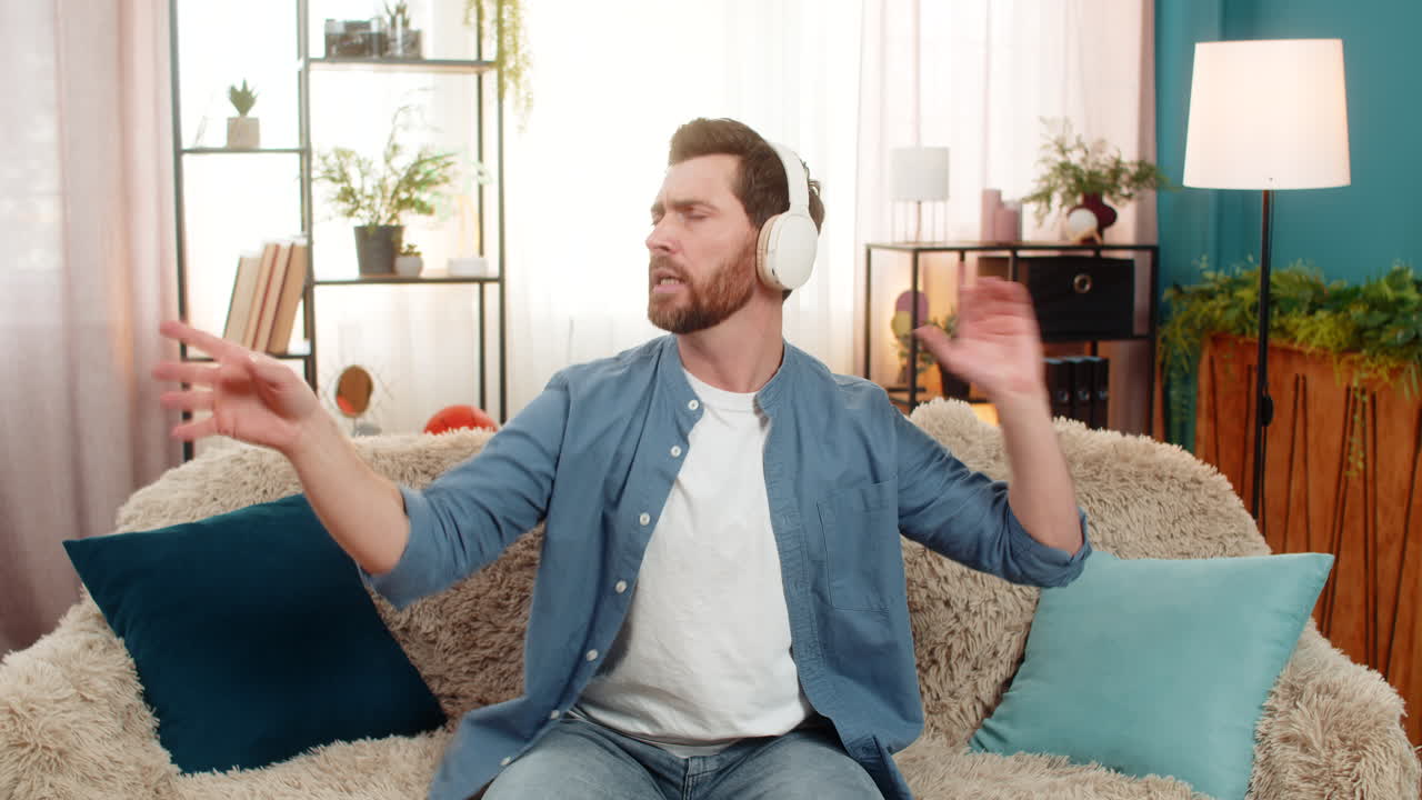 Young man wearing headphones raises hands like conducting orchestra deeply immersed in music rhythm