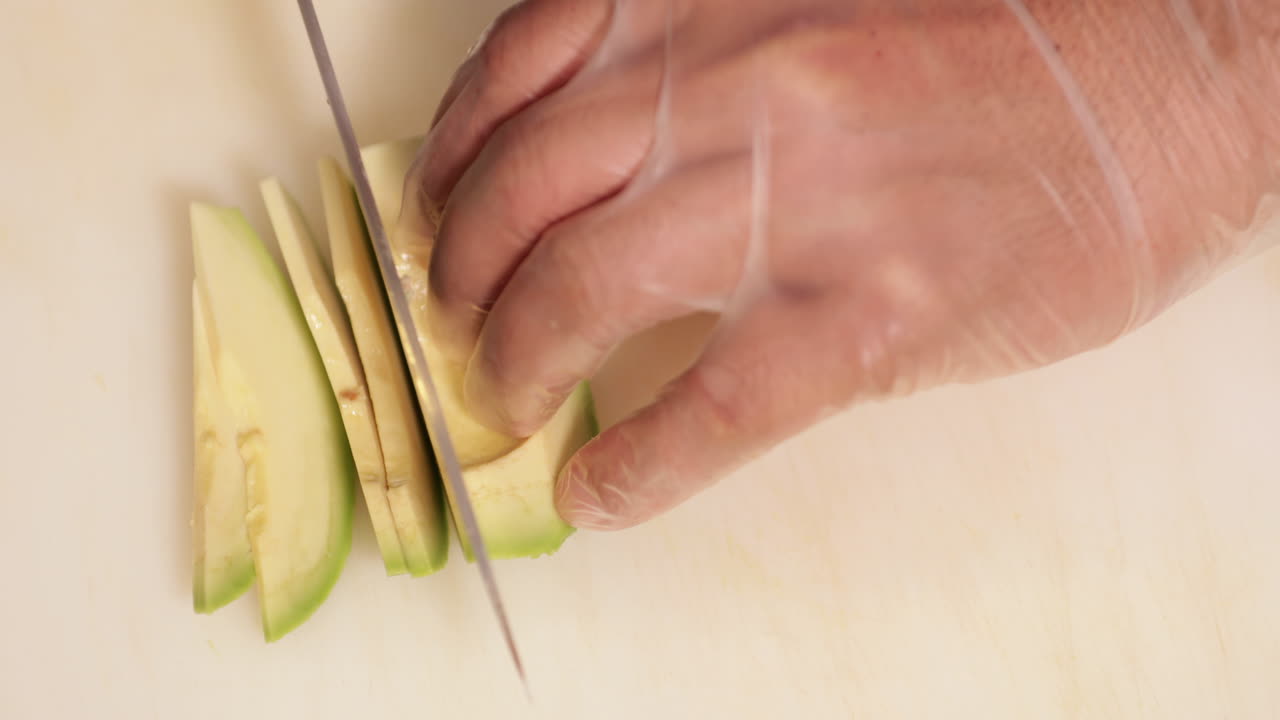 chef de sushi cortando aguacate en una tabla de cortar blanca para un plato de sushi en la cocina