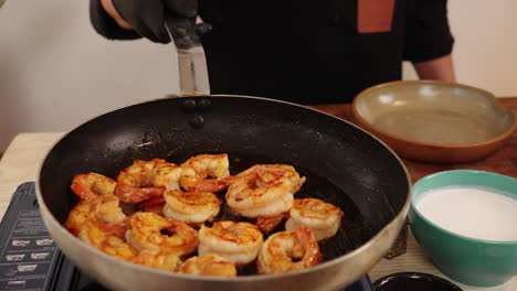 Zoom-out-shot-while-chef-swirling-the-shallow-frying-pan-with-yummy-peeled-prawns-cooking-on-butane-gas-stove-in-slow-motion