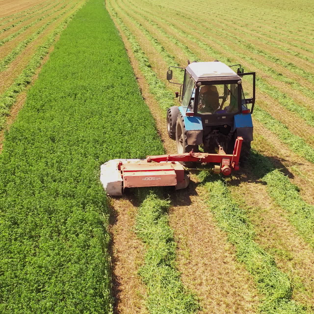 Aerial view of tractor in the field in summer. Special technology for mowing green grass in process on the field background in sunny day.