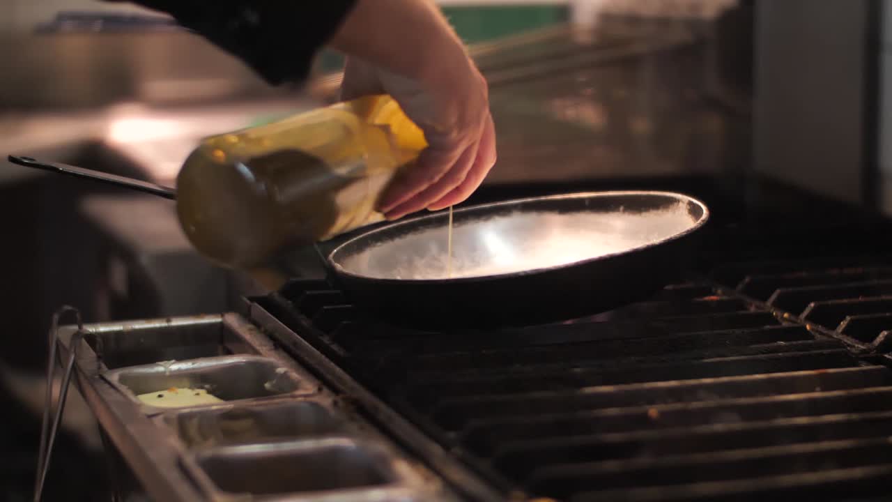Chef pouring oil on frying pan. Close up shot