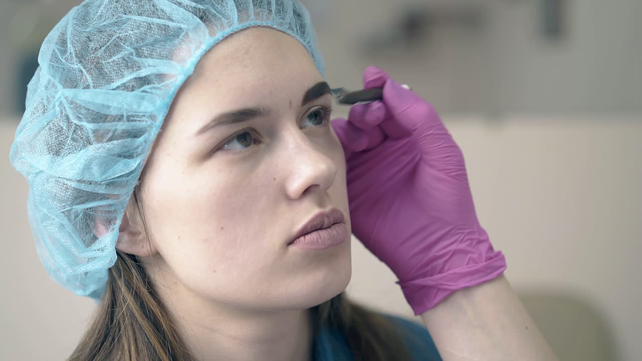 el maestro cepilla la ceja de la chica con un tatuaje fresco en el salón