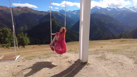 a girl in a pink dress on a swing against the background of the high caucasus mountains