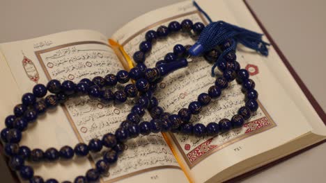 an open quran lying on a table with a prayer beads lying on it, the shot approaches the quran