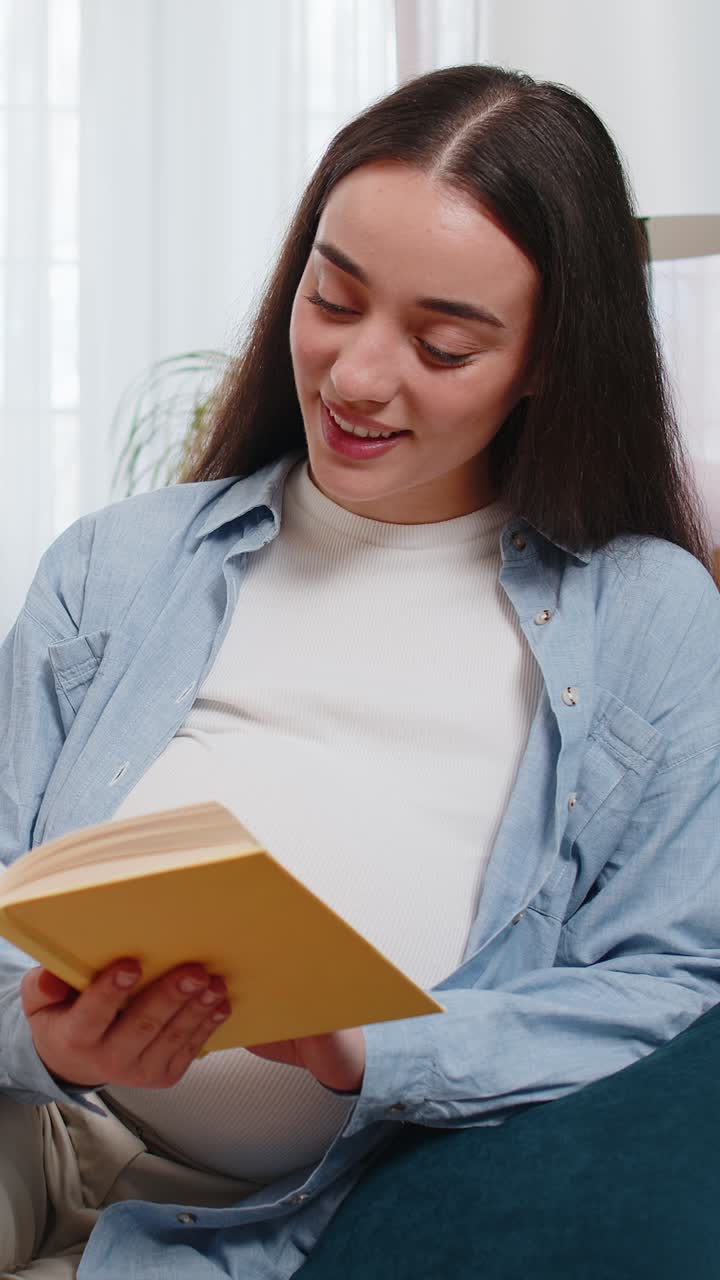 Pregnant caucasian woman reading book advice child care guide feeling relax on cozy couch at home