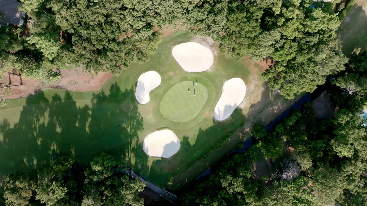 Aerial view of a lush golf green surrounded by four sand bunkers and trees, capturing Hilton Head’s scenic and refined golfing landscapes