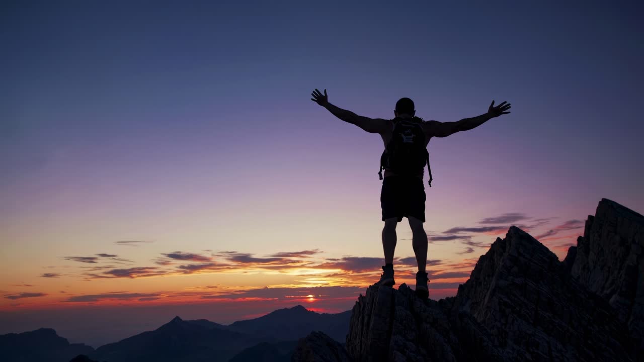 Un video que muestra a un excursionista silueteado contra un vibrante atardecer en la cima de una montaña, transmitiendo libertad.