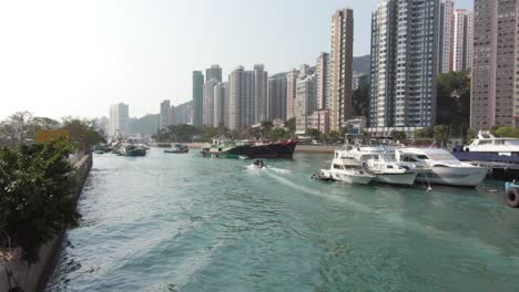 Boats anchored in a Hong Kong canal with skyscrapers in the background.