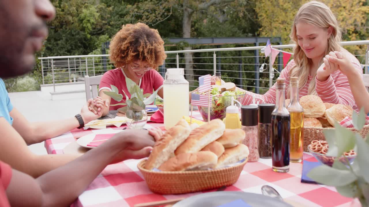En gruppe ulike venner holder hender og ber ved middagsbordet i hagen, sakte film