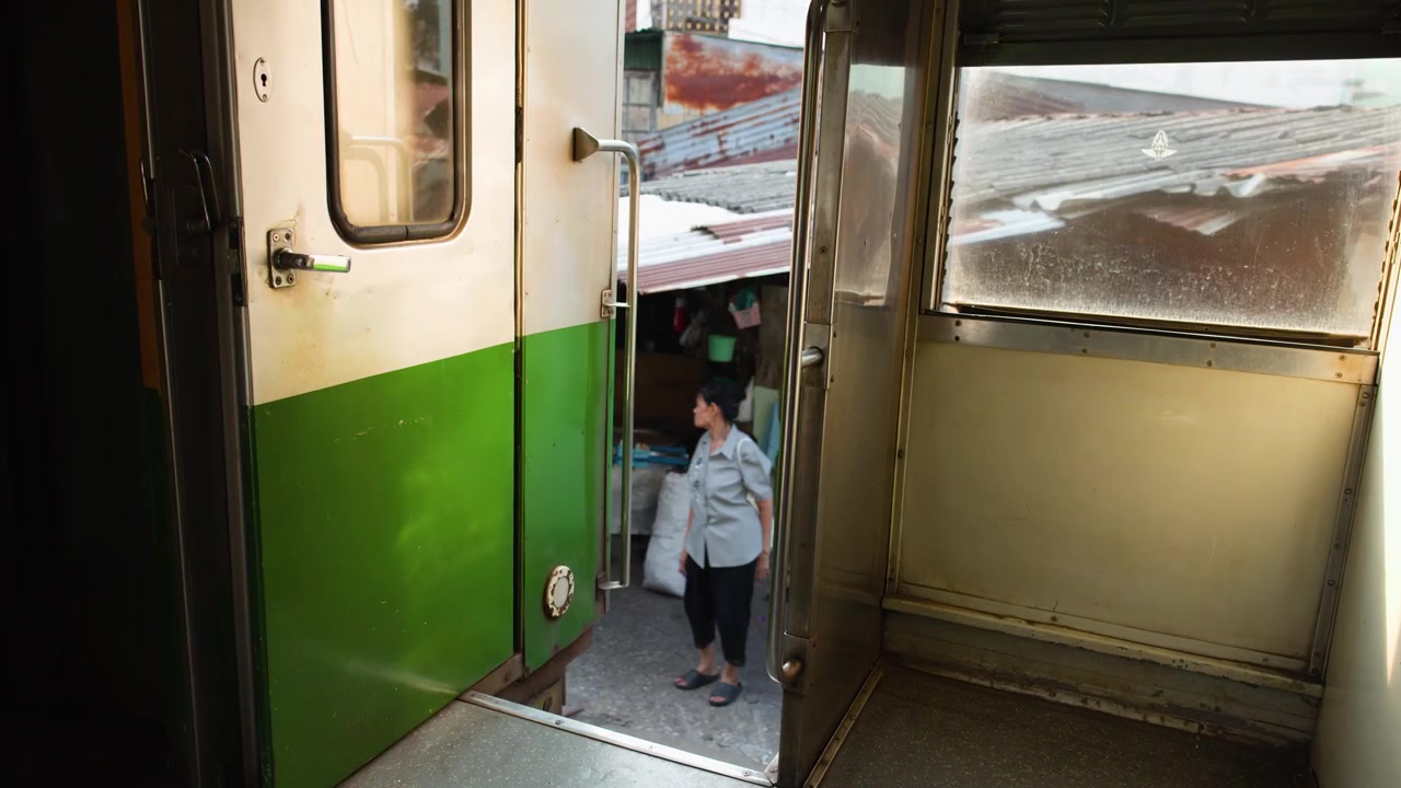 Inquadratura interna statica da un vagone di treno in movimento che passa accanto a tetti di lamiera ondulata a Bangkok