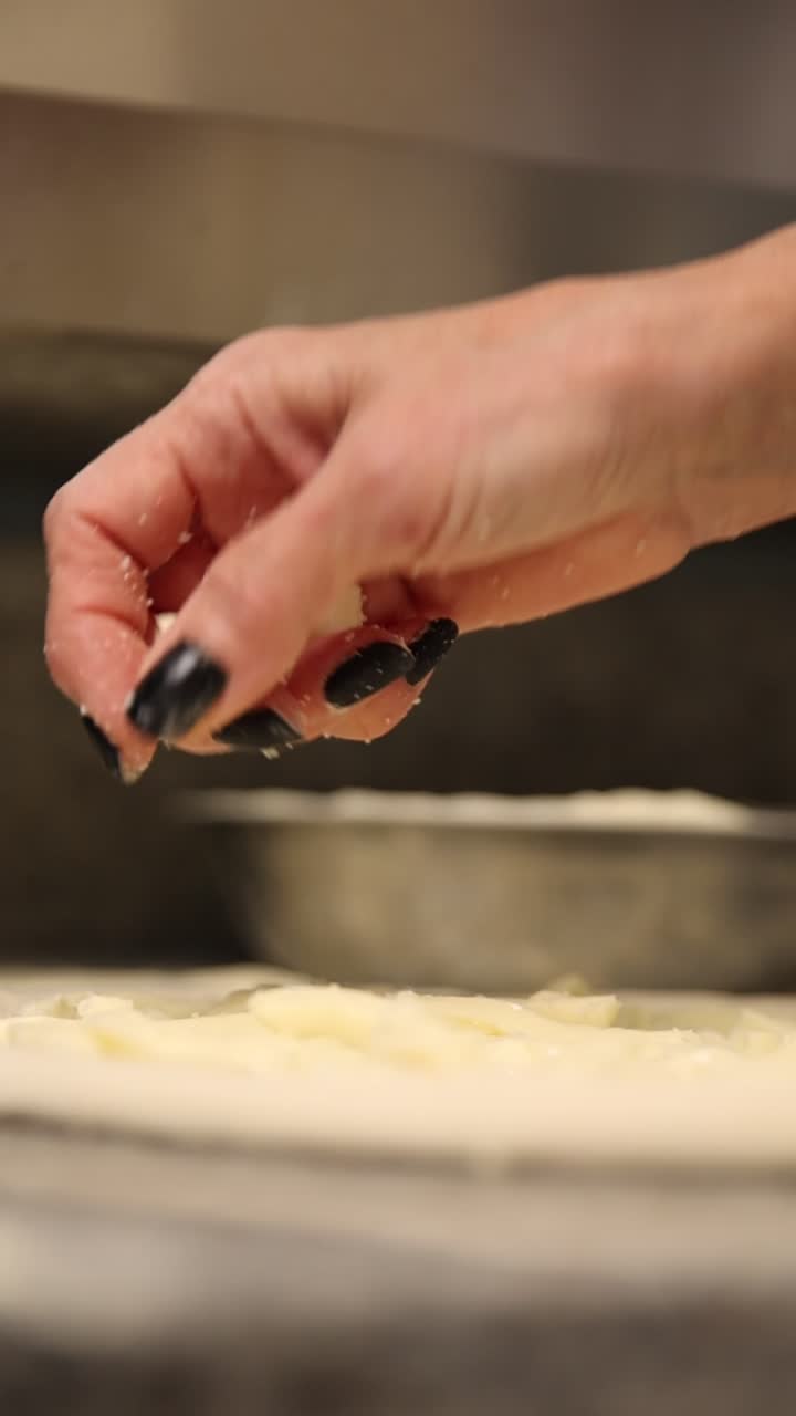 Primo piano di mano che cosparge formaggio su impasto per pizza