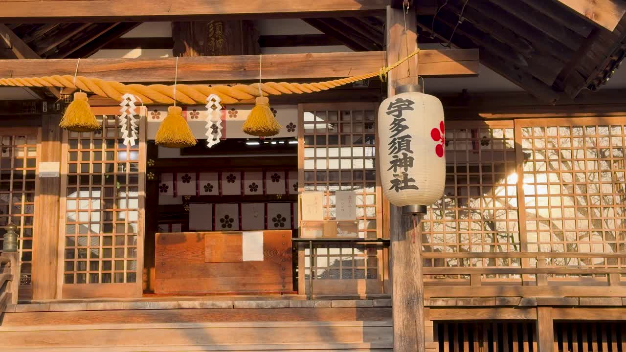 Static medium shot of a Shinto temple facade with paper lanterns and shimenawa rope