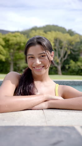 vertical video portrait of smiling biracial teenage girl standing in sunny pool, slow motion