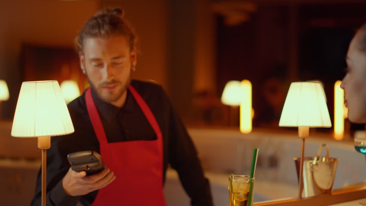Handsome man ordering whiskey in bar. Woman making contactless payment in club