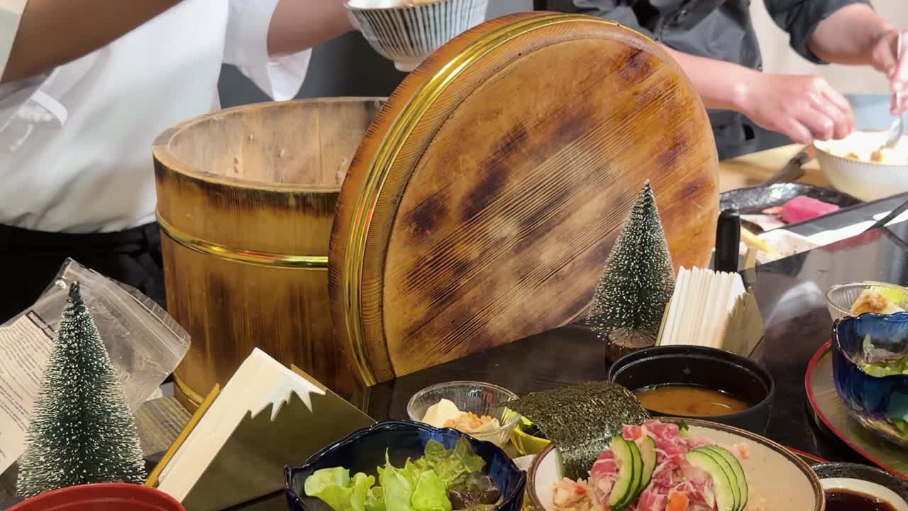 カラフルなおまかせ丼の横で、大きな木桶の中でご飯を扱うシェフのクローズアップ