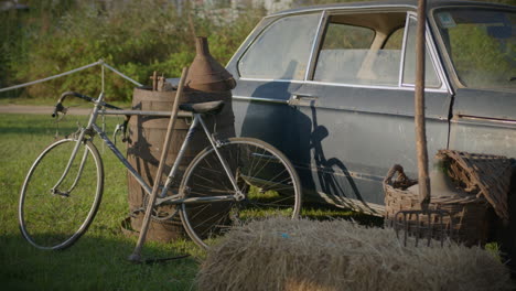 old and rusty car surrounded by rustic farm tools and old bicycle