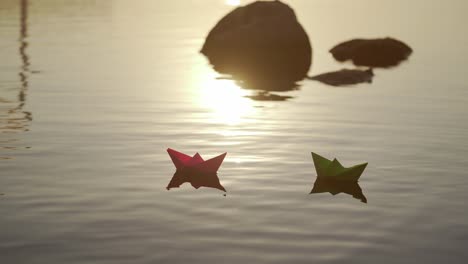homemade origami boats at sunset. two paper ships floating in the river among stones in the evening. dreams and freedom concept.