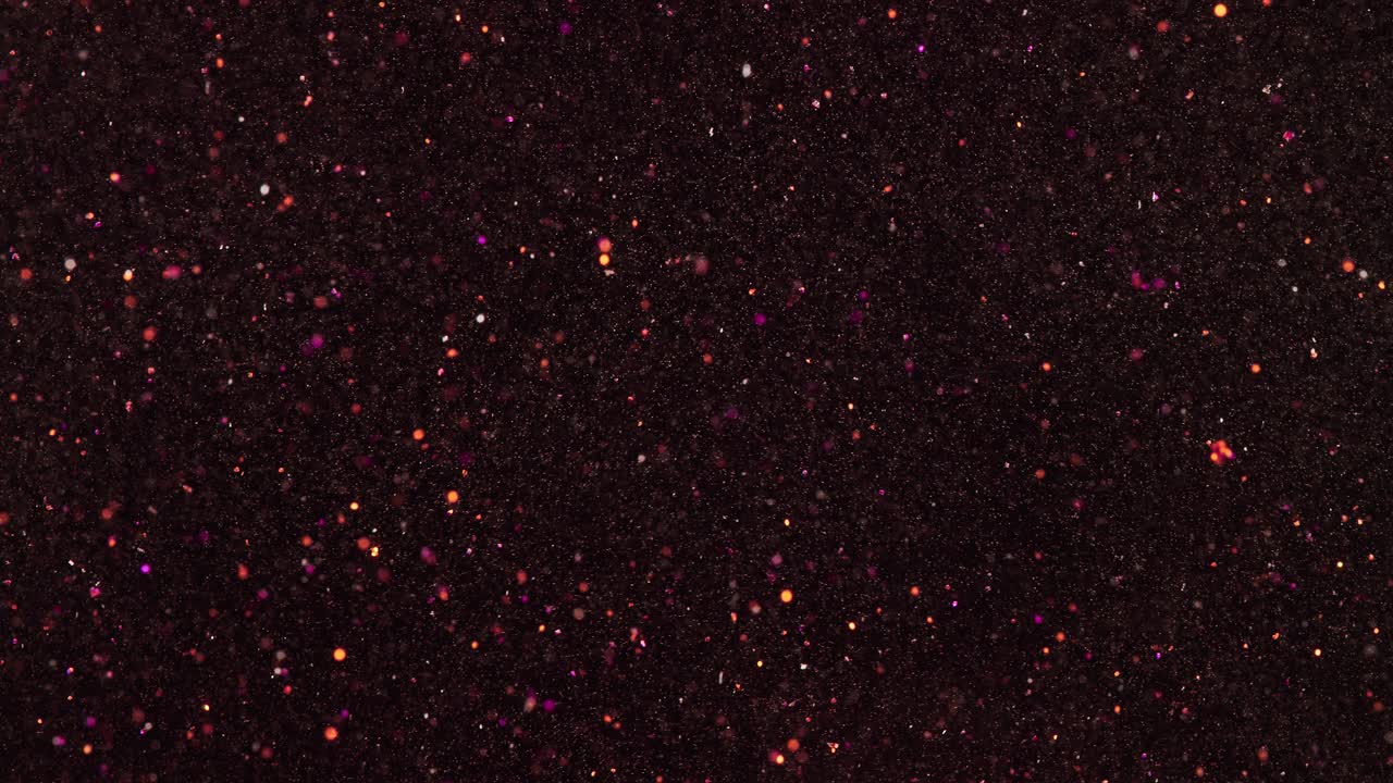 en cámara lenta, las partículas de brillo rosa y dorado se mueven casi al azar sobre un fondo negro